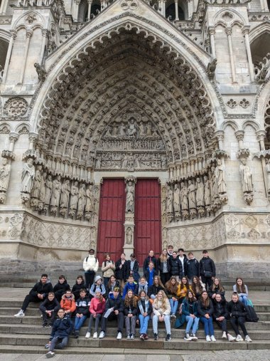 Die deutschen und französischen Schüler*innen sitzen vor dem Eingang der Notre Dame und lachen in die Kamera.